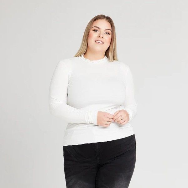 Langærmet hvid top med diskret blondedetalje, matchet med sort buks, fra plus size-kollektionen.