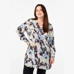 Trendy plussize blomstret tunika i pastelfarver, med lange ærmer og V-hals, præsenteret i et casual stilfuldt look.