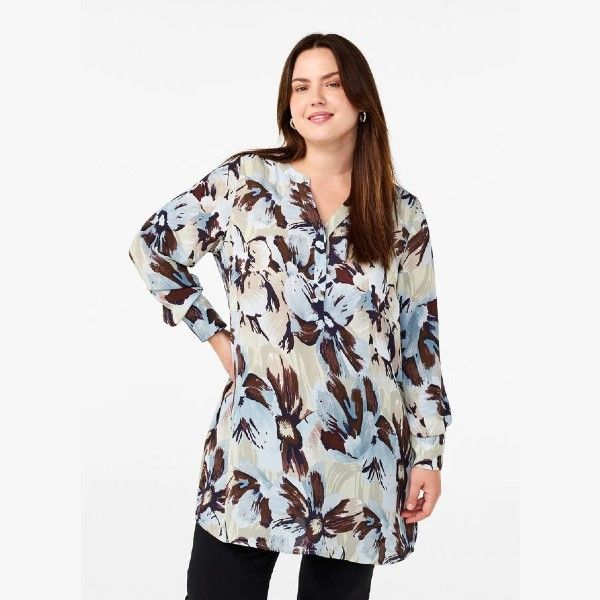 Trendy plussize blomstret tunika i pastelfarver, med lange ærmer og V-hals, præsenteret i et casual stilfuldt look.