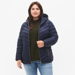 Plussize dynejakke i marineblå med hætte og lynlås, kombineret med grøn sweater og lyseblå jeans.