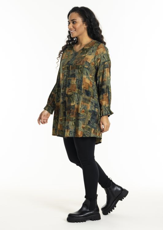 Plussize tunika i efterårsfarvet print kombineret med sorte leggings og chunky støvler, perfekt til moderne hverdagslook.