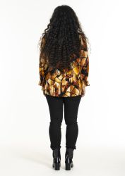 Mønstret bluse i plussize med sort bukser og høje hæle står med ryggen til kameraet for et minimalistisk baggrund.