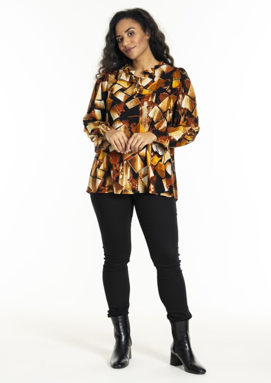 Mønstret bluse i efterårsfarver og sorte slim-fit bukser med sorte ankelstøvler på hvid baggrund.