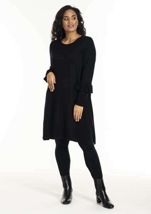Sort A-formet kjole med lange ærmer og flæsedetaljer, kombineret med sorte leggings og højhælede støvler.