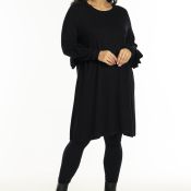 Sort A-formet kjole med flæseærmer, kombineret med sorte leggings og ankelstøvler, perfekt til både hverdags- og festbrug.