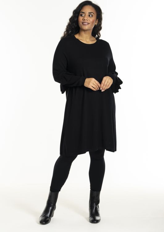 Sort A-formet kjole med flæseærmer, kombineret med sorte leggings og ankelstøvler, perfekt til både hverdags- og festbrug.