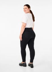 Sorte plussize stretch-jeans med høj talje og et klassisk look, stylet med en hvid t-shirt og tykke sorte sko.