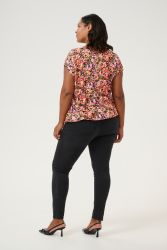Farverig blomstret bluse og sorte slim-fit jeans stående med ryggen til kameraet og ser over skulderen.