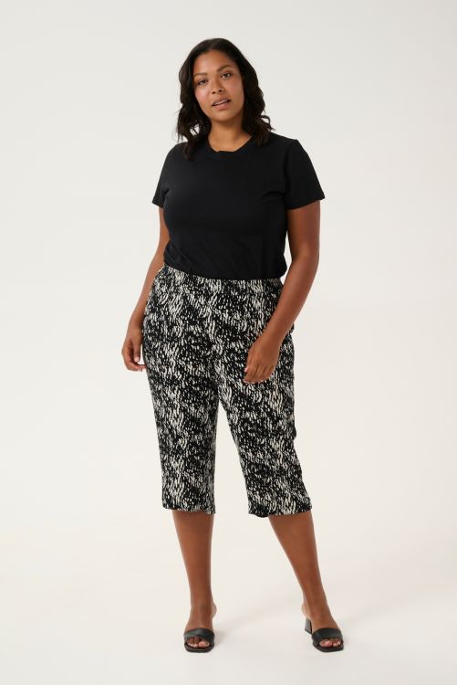 Moderne sort plussize t-shirt med enkle linjer kombineret med mønstrede capri-bukser i sort og hvid. Komplet look til afslappet elegance.