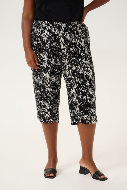 Mønstrede capribukser i plussize med elastisk talje og sort top, akkompagneret af sort åben fodtøj.