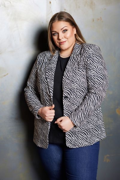 Plussize zebra-printet jakke i sort og hvid med knapper, kombineret med en enkel sort top og blå jeans.