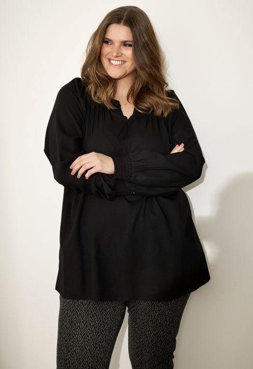 Sort plussize tunika med v-hals og løse ærmer kombineret med mønstrede bukser, perfekt til hverdags- eller arbejdstøj i stor størrelse.