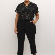 Plussize sort prikket bluse med flæseærmer og snørredetalje samt sorte bukser og højhælede sko for stilfuldt hverdagstøj.