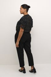 Sort prikket bluse og sorte bukser i plussize, sidemodel stil med trendy sko.