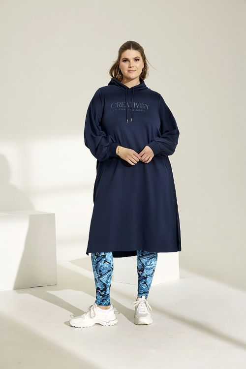 Plussize hættetrøje i navy med tryk og mønstrede leggings med hvide sneakers stående i en lys studieindstilling.