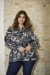 Elegant plussize bluse med bladprint og snøre i taljen, præsenteret foran en murstensvæg, perfekt til både hverdag og kontor.