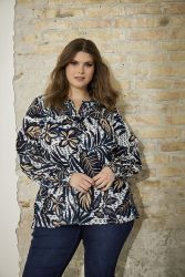 Elegant plussize bluse med bladprint og snøre i taljen, præsenteret foran en murstensvæg, perfekt til både hverdag og kontor.