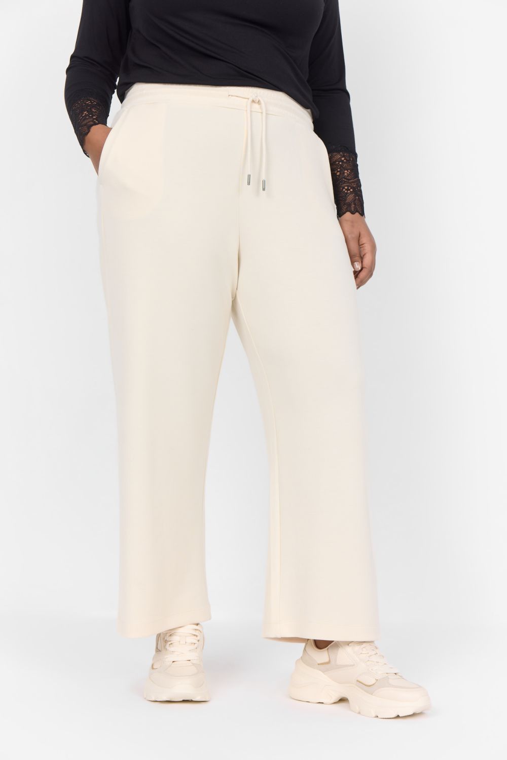 Beige plussize bukser med snøre og lige ben, stylet med sorte detaljer og beige sneakers.