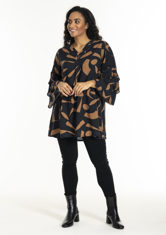 Mønstret plus size tunika med lange ærmer og sorte skinny jeans, kompletteret med sorte ankelstøvler.