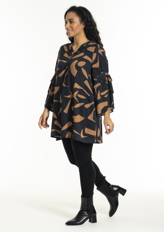 Moderigtig plussize tunika med abstrakt print, matchet med sorte leggings og elegante ankelstøvler.