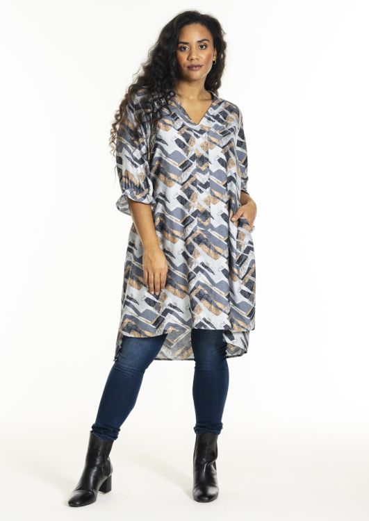 Plussize tunika med geometrisk mønster i blå og beige nuancer, kombineret med mørkeblå jeans og sorte ankelstøvler.