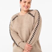 Beige plussize striktrøje med unikke sorte pyntesømme langs ærmerne, kombineret med en klassisk jeans.