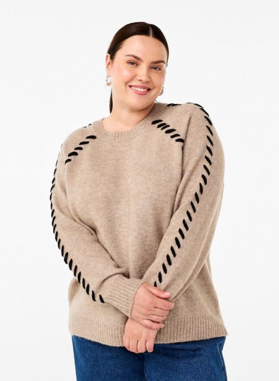Beige plussize striktrøje med unikke sorte pyntesømme langs ærmerne, kombineret med en klassisk jeans.