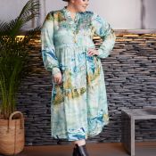 Plussize mønstret kjole med lange ærmer og krave, præsenteret i et moderne miljø med stenbaggrund og planter.