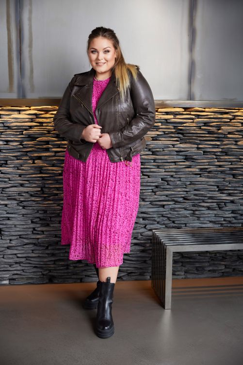 Plussize outfit med læderjakke og lyserød plissé-kjole kombineret med sorte ankelstøvler.