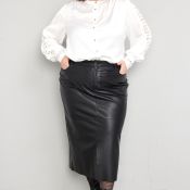 Outfit med hvid bluse med knapper og detaljeret ærmekant, samt sort læderlook nederdel og sorte støvler.