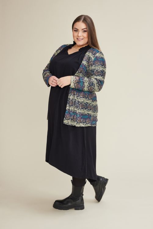 Plussize outfit med sort kjole og mønstret cardigan komplementeret af sorte støvler, egnet til både arbejde og fritid.