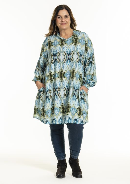 Plussize tunika med etnisk mønster og trekvartærmer, kombineret med mørke slim jeans og sorte støvler.