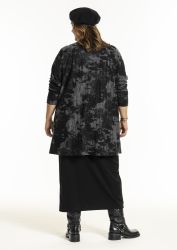 Elegant plussize outfit med flerfarvet tunika og sort nederdel, kombineret med moderne sorte støvler og baret.