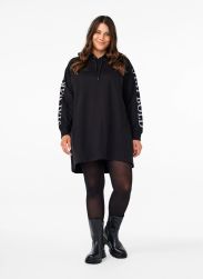 Sort hættetrøje fra Zizzi i plussize med logoprint på ærmerne, kombineret med strømpebukser og læderstøvler.