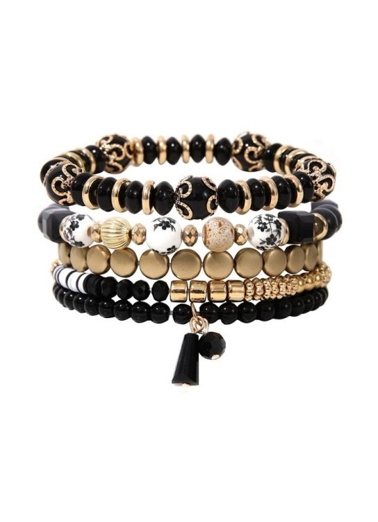 Stack af armbånd i sort og guld med forskellige perlemønstre og vedhæng, ideel til accessorizing.