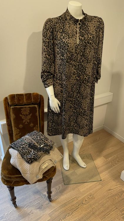 Leopardmønstret plussize kjole på mannequin ved siden af en antik stol med foldet tørklæde.