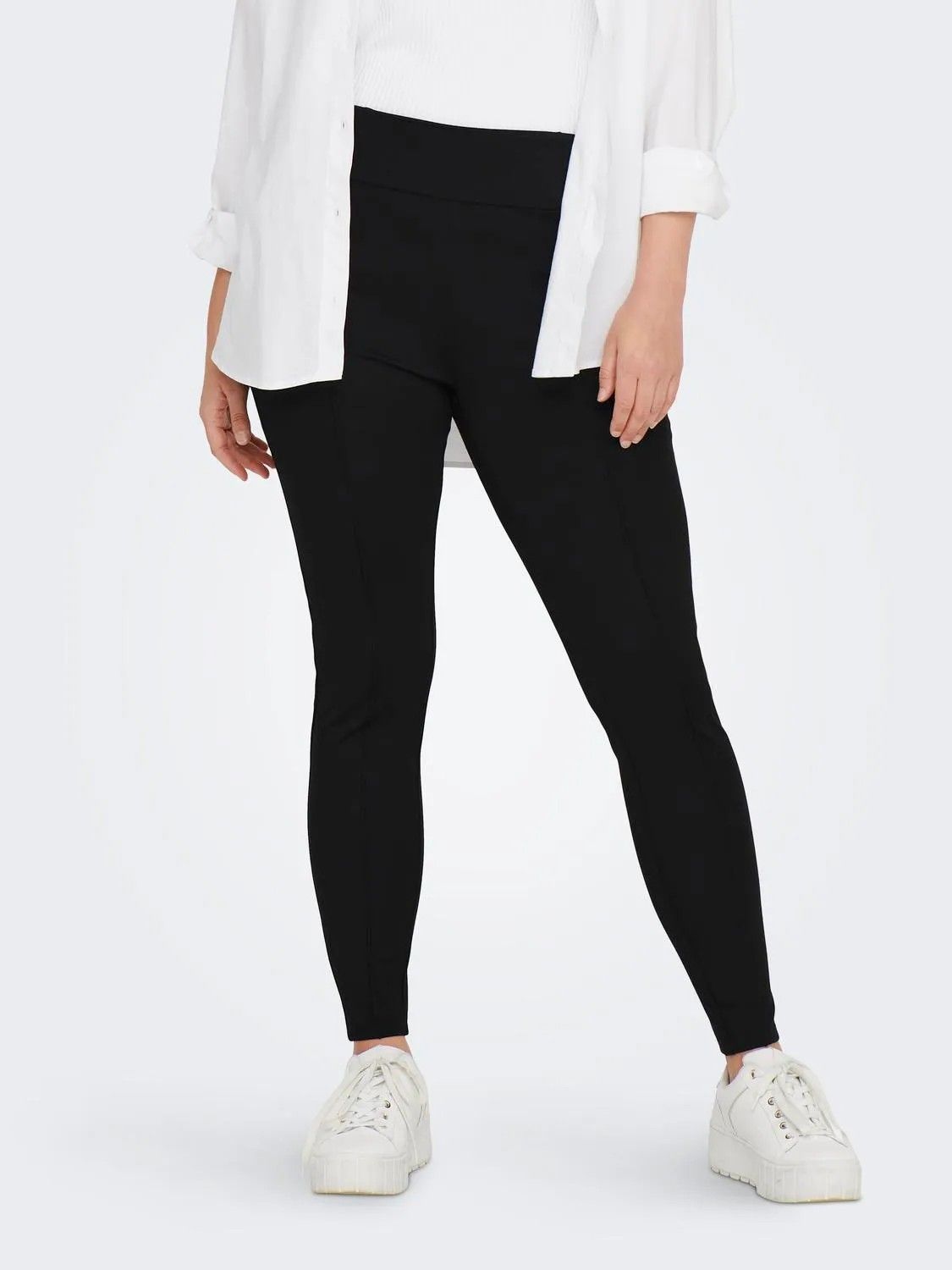 Sorte plussize leggings med høj talje præsenteret med hvid skjorte og hvide sneakers.