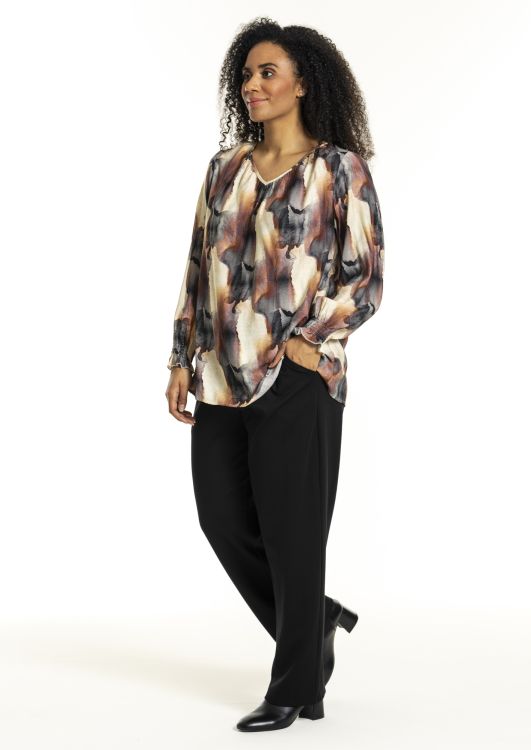Plussize Studio bluse med abstrakt mønster og sorte bukser på hvid baggrund, ideelt til moderne kontor- eller aftengarderobe.