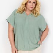 Pastelfarvet bluse med korte ærmer og V-udskæring på model, kombineret med lyse bukser, egnet til plussize mode.