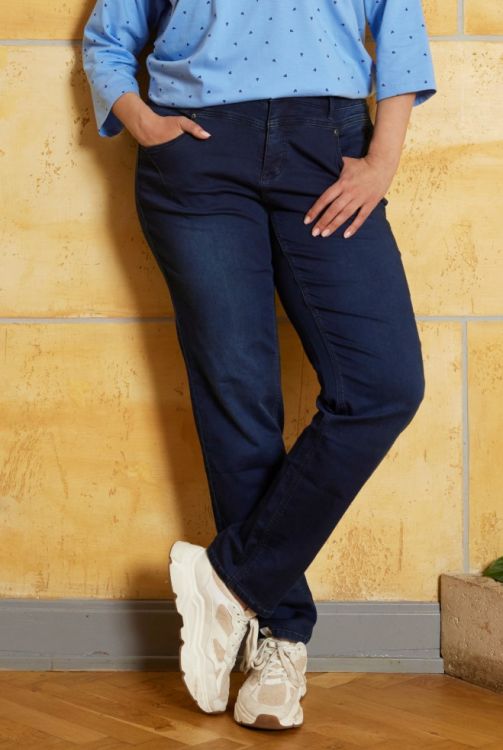 Moderne mørkeblå jeans med afslappet pasform og hvidt fodtøj, præsenteret i et stilet indretningsmiljø.