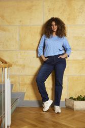 Moderigtigt plussize outfit med prikket bluse og marineblå jeans, præsenteret i et indendørs miljø med trægulv og gul væg.