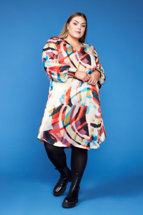 Farverig plussize kjole med abstrakt mønster, præsenteret mod blå baggrund, perfekt til forskellige anledninger.